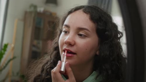 Young Woman Applying Lip Gloss in Mirror