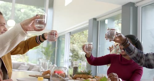 Amigos diversos estendendo os braços, tostando copos na mesa, bebendo água, servindo salada, espaço para cópias