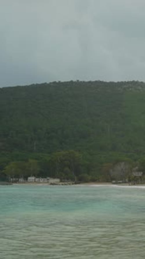 Vertical video. Overcast, cloudy weather over hills with dense forests, waves on the sea.