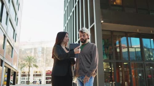 Coworkers Reviewing a Tablet Outside Office Buildings
