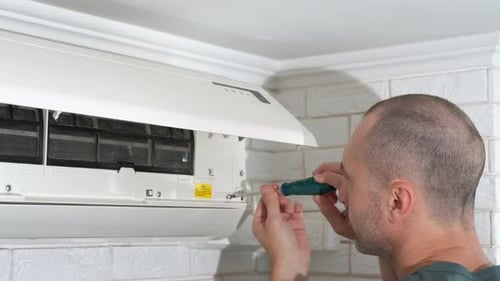 Man Repairing Air Conditioner Unit with Screwdriver