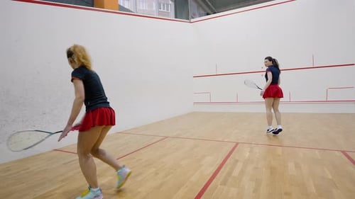 Couple of Young Women Plays Squash on Fourwalled Court