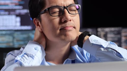 Close Up Of Programmer Stretching While Writing Code By A Laptop Using Multiple Monitors