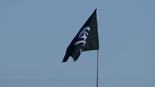 Waving Black Pirate Flag with Skull Against Blue Sky