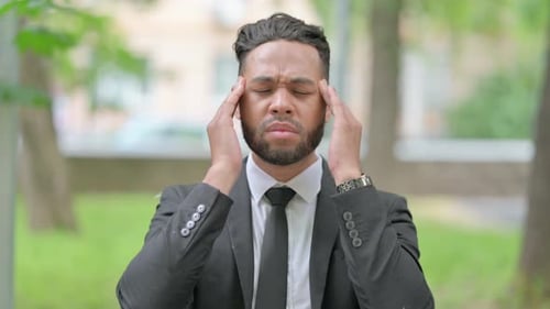 Stressed Man in Suit Rubbing Temples Outdoors
