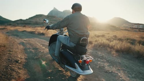 Man Rides Scooter on Dirt Road at Sunrise