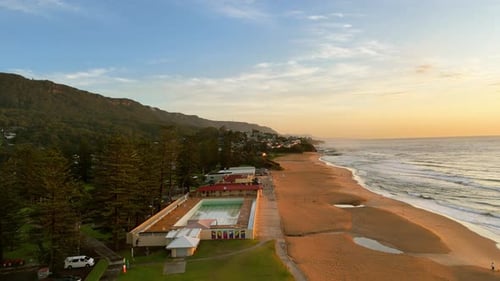 Aerial Overview of Thirroul Beach at Sunrise With Pool, Pines and Rolling Waves