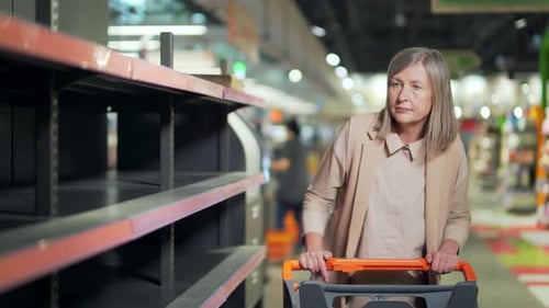 Senior woman shopper in supermarket, grocery store near empty shelves counters. Elder Mature female