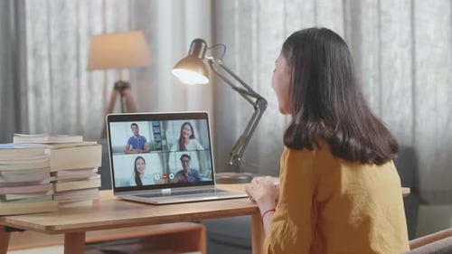 Side View Of A Young Female Waving Hand For Greeting While Studying On Zoom By A Laptop At Home