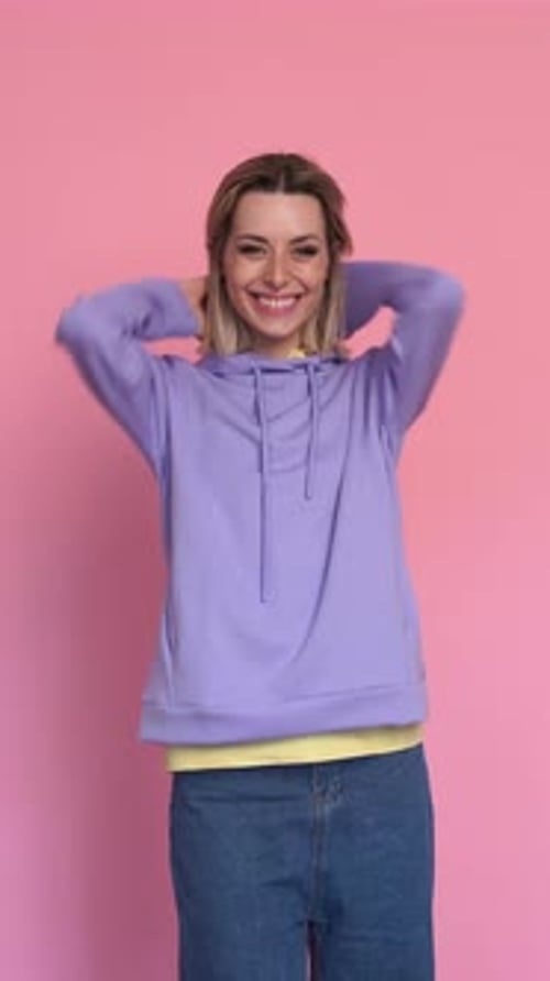 Smiling Woman in Hoodie Posing Against Pink Background