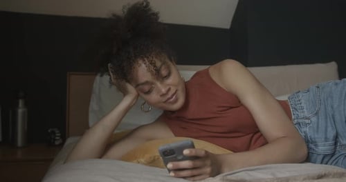 Young Woman Laying on Bed Using Smartphone