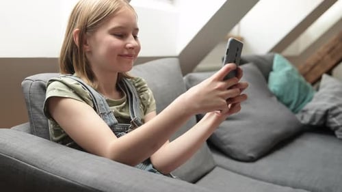 Smiling Child Using Smartphone on Couch at Home