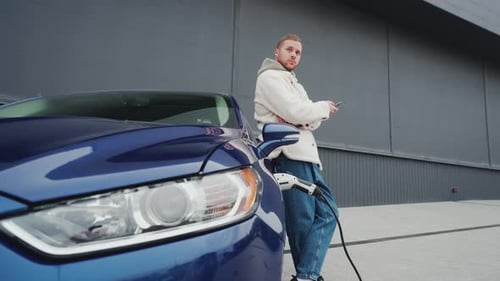 Young Man Charging Electric Car Using Cellphone