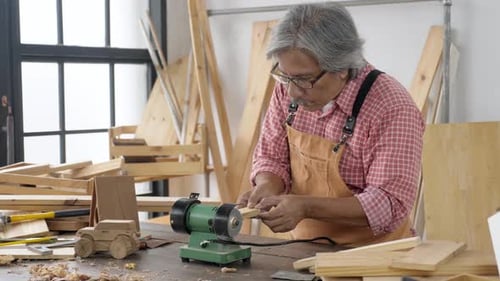 dark skin, grey hair, senior Asian man doing woodwork at workshop studio