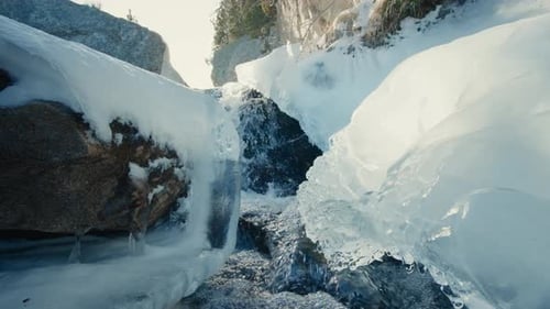 Gebirgswasserstrom, der am sonnigen Frühlingstag durch Eis fließt, Schmelzwasser