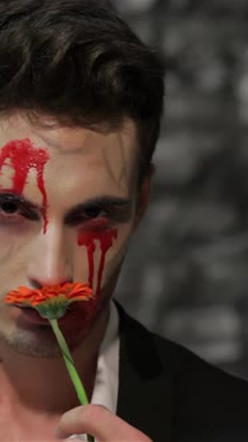 Man with face makeup posing with a flower
