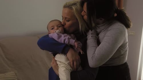 Happy lesbian couple having tender moments with their small baby at home
