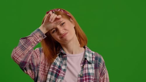 Tired woman suffering from stress touching her forehead on a green screen background.