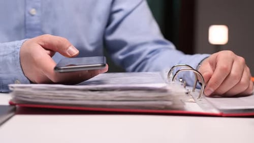 Person Uses Smartphone While Working With Documents