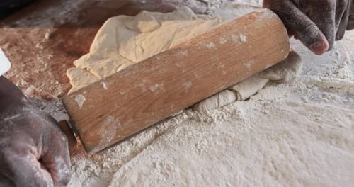 Midsection of african american male baker working in bakery kitchen, rolling out dough, slow motion