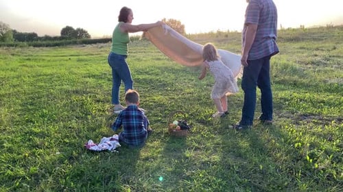Charming Family with Two Kids Organizing Small Pictin on Meadow at Sunset