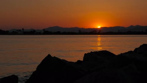 Golden Sunset Over Ocean Rocks and Distant Mountains