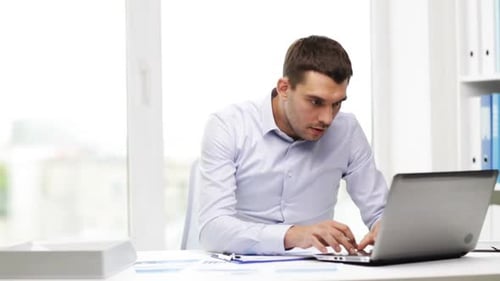Busy hispanic businessman works with laptop and papers in office environment