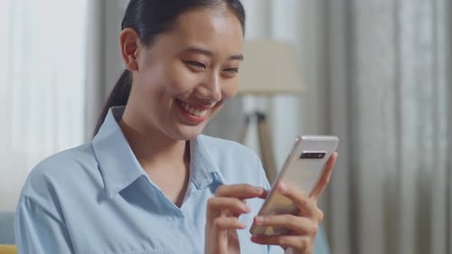 Close Up Of Asian Woman Enjoys Using Smartphone While Sitting On Sofa In The Living Room