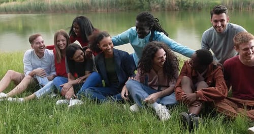 Multiethnic Friends Having Fun Together Sitting on Grass Next to the Lake