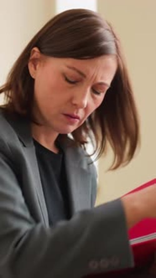 Businesswoman Organizing Papers Into Red Folder in Office Environment