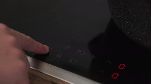 Hand pressing power button on induction cooktop panel. Close-up view in a modern kitchen. Technology