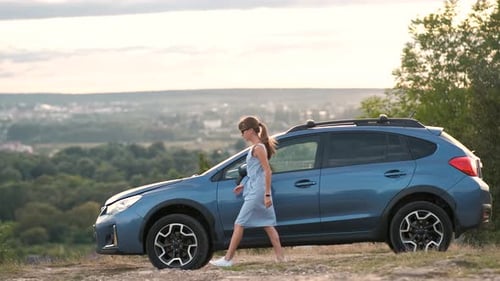 Young Female Driver Standing Near a Broken Car with Open Up Hood Inspecting Her Vehicle Engine and