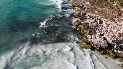 Aerial View of Rocky Shoreline Against Turquoise Sea Waves in Daylight