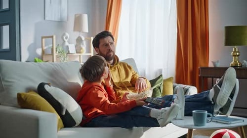 Father and Son Relaxing on Couch, Watching TV