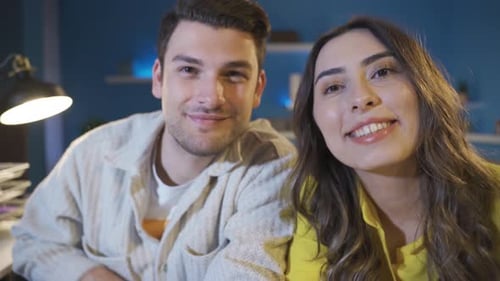 Smiling Couple Waving Cheerfully at Camera in Home