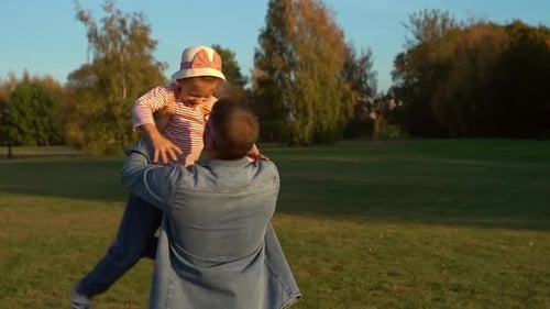 Glücklicher Familienvater hebt Tochter auf die Hände und dreht sich bei Sonnenuntergang im Herbstpark