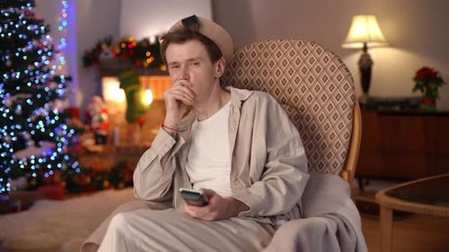 Disinterested Man Yawning Switching TV Channels with Remote Control Looking at Camera