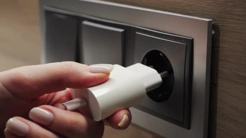 Nahaufnahme des Einsteckens eines elektrischen Steckers von Hand in die Wandsteckdose zum Anschließen einer Stromquelle für