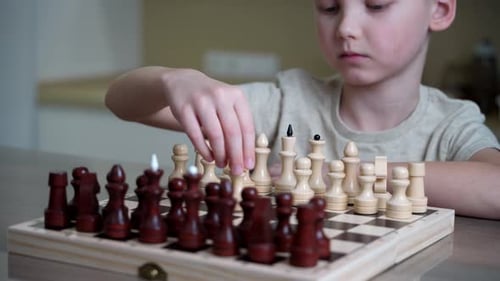 Child Plays Chess Board Game at Table