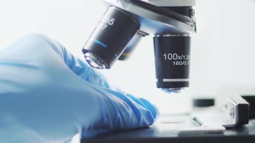 Close Up of Microscope and Gloved Hand Adjusting Slide