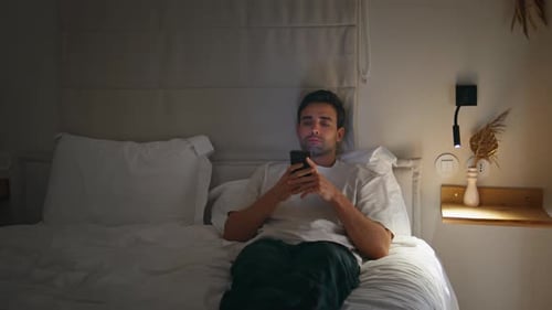 Man Relaxing in Bed While Using Phone