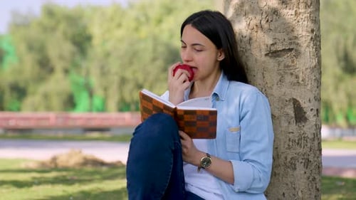 Woman Eating Apple and Reading by a Tree