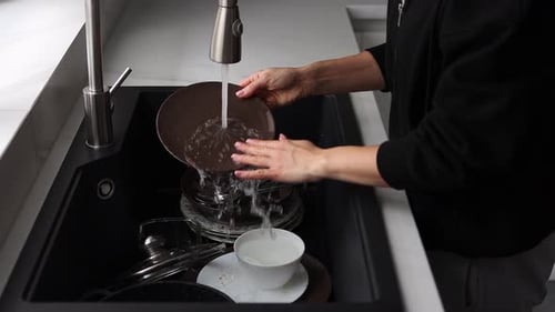 Close-up of a woman washing dishes in a modern black kitchen sink. Domestic chores and daily life