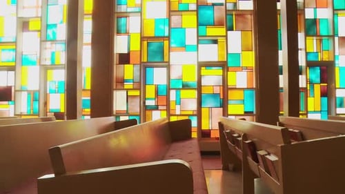 Dolly shot of rows of empty church pews framed by a stunning stained glass window wall blossoming wi