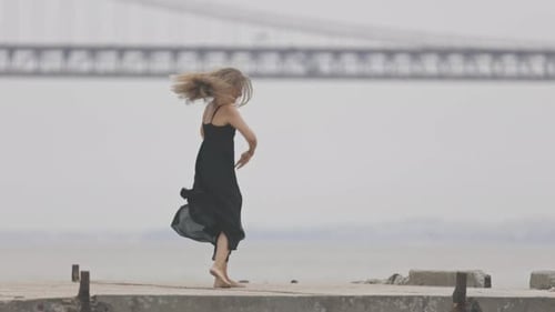 An Adult Smiling Woman in Black Dress Dancing on the Pier