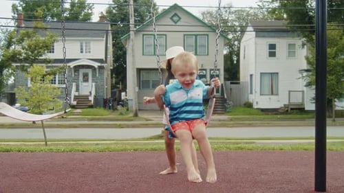Siblings Enjoy Summer Fun On A Playground As Sister Swings Her Little Brother