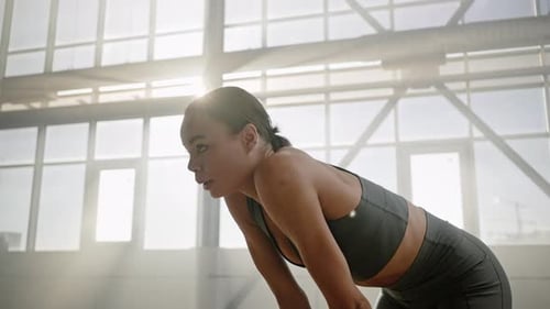 Athletic Woman Engaged in Sports Routine Relaxing After Heavy Training in a Smokey Gym Interior