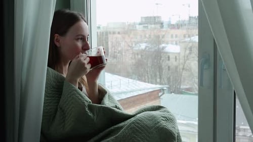 Woman Drinks Hot Drink by Window Seat