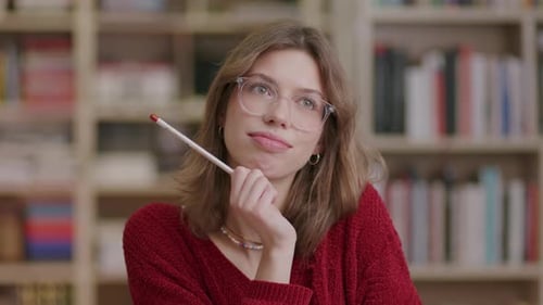 A young beautiful female student holding pencil reacts to an idea in the library—medium shot.