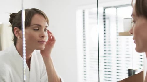 Woman Applies Face Cream in Bathroom Mirror